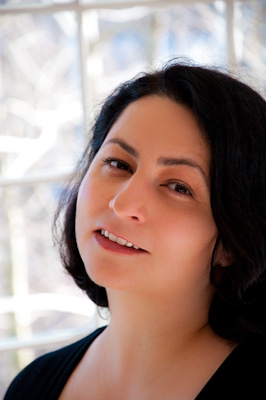 In Kirun Kapur's headshot a woman with dark hair smiles at the camera.